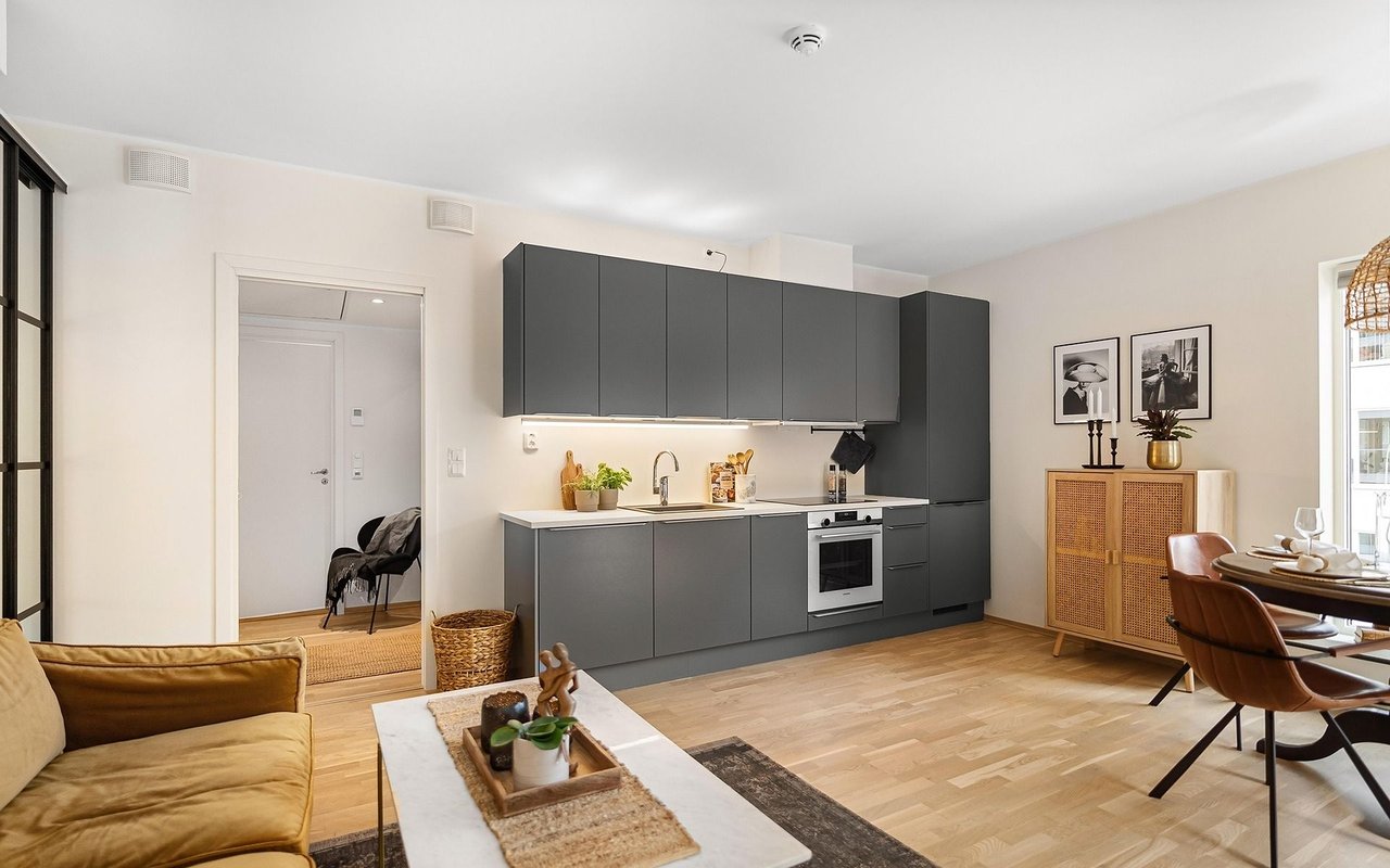 Open-plan kitchen with charcoal cabinets, light wood floors, and an adjoining mustard-sofa living area.