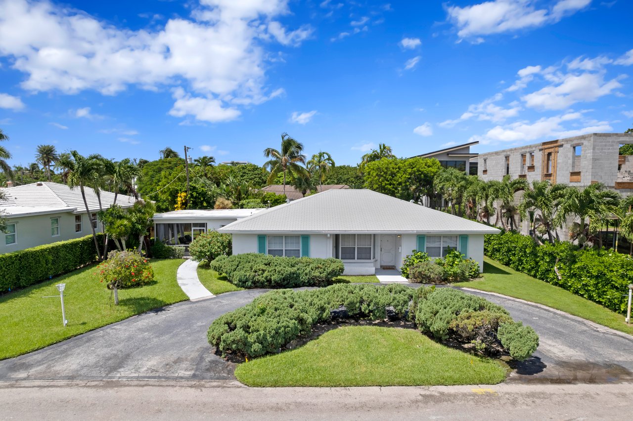 Single-story home with turquoise shutters, a curved driveway, and landscaped lawn.
