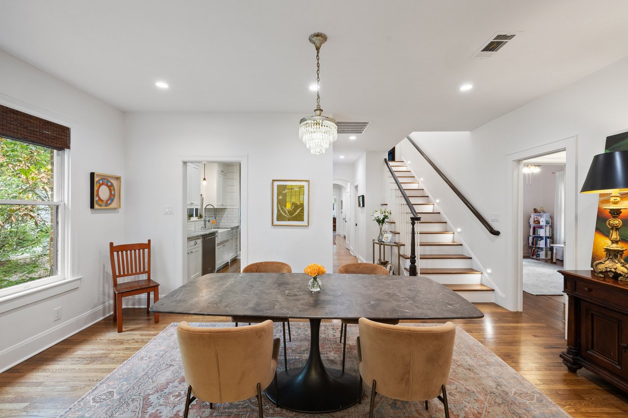 Dining area with a stone table, crystal chandelier, and staircase beside the kitchen.