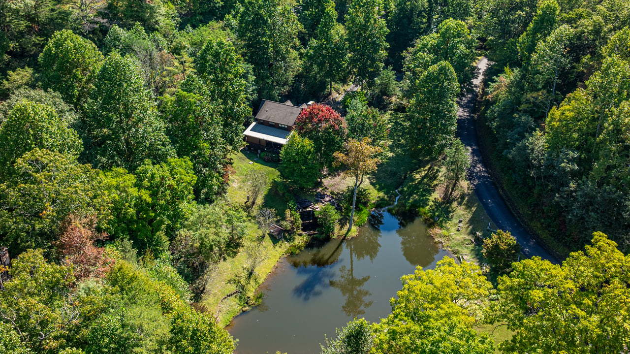 Aerial view of a wooded mountain home beside a pond off Pilot Knob Road in Glenville, NC