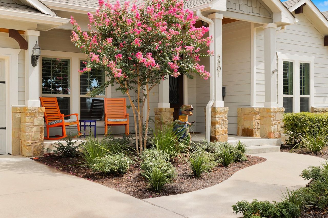 House entry with stone porch columns, orange chairs, and a pink-flowering crepe myrtle.