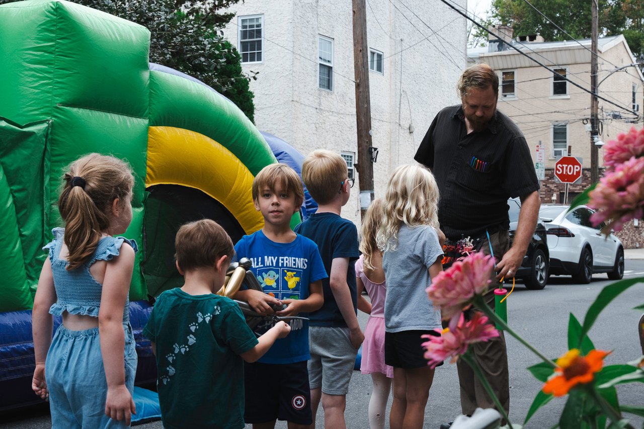 Children gather beside a green and yellow bounce house as an adult supervises the block party.