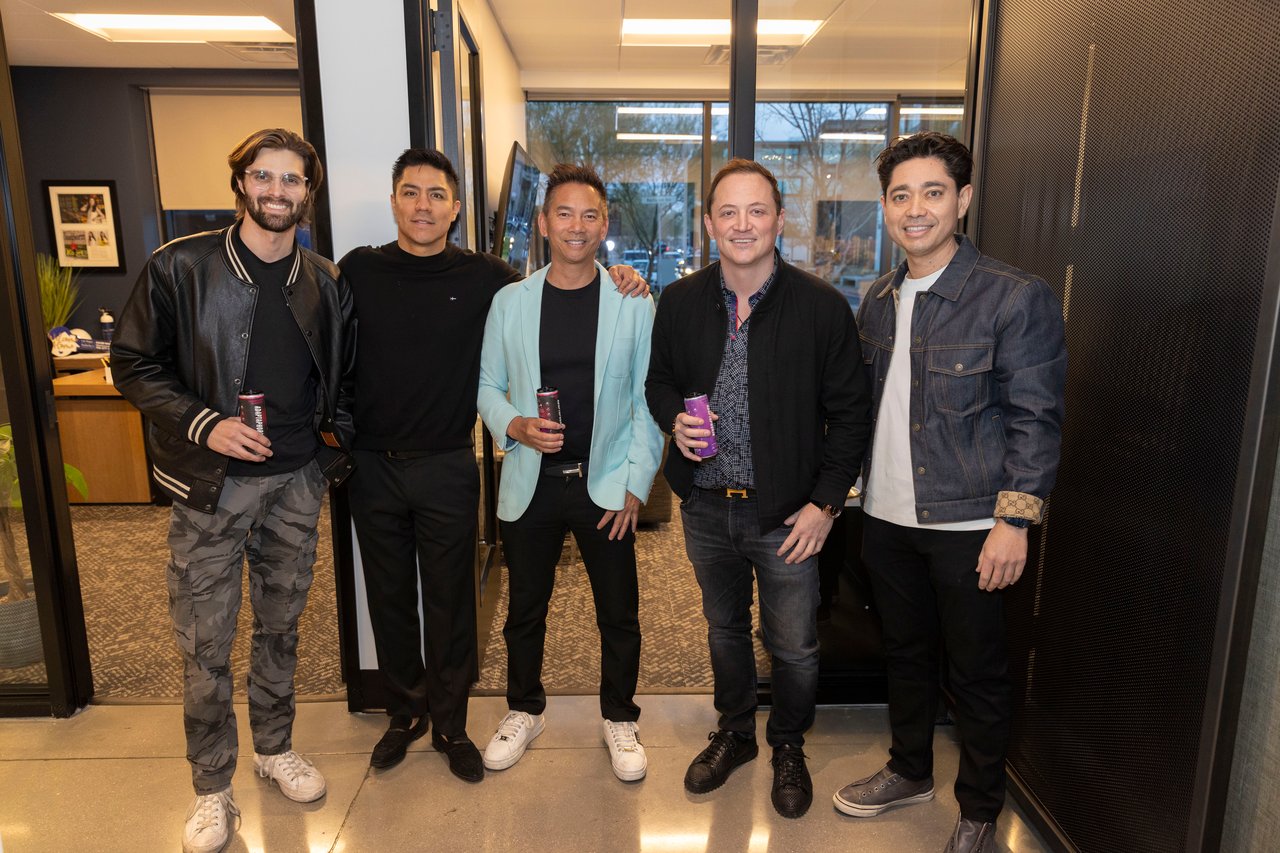 Five men pose in an office lobby, several holding drinks.