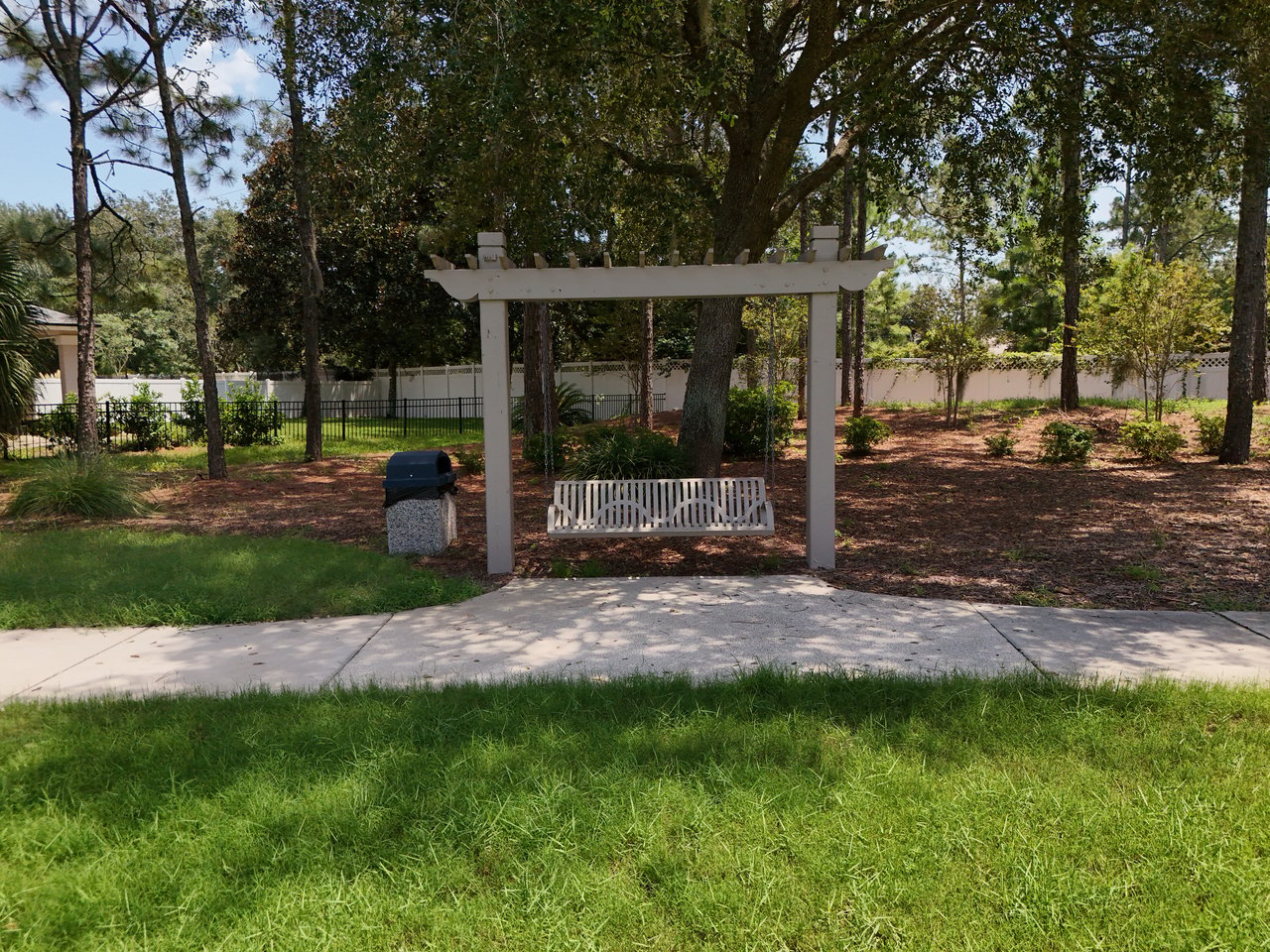 Pergola with a hanging bench swing in a shaded, landscaped outdoor seating area.