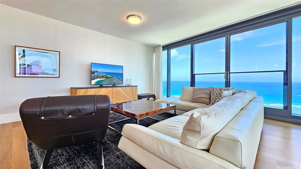 Living room with a white sectional and floor-to-ceiling windows overlooking the ocean.