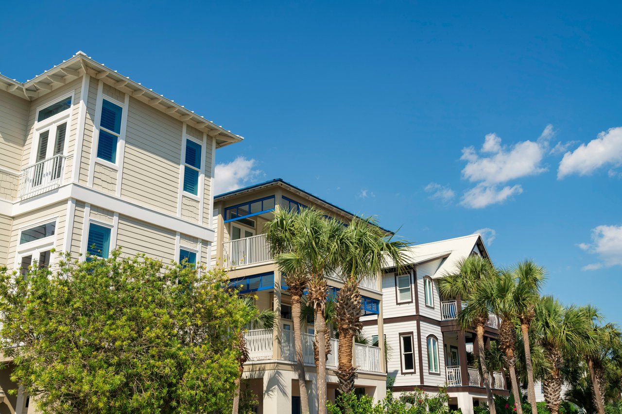 Coastal condominiums with balconies and palm trees beneath a bright blue sky.