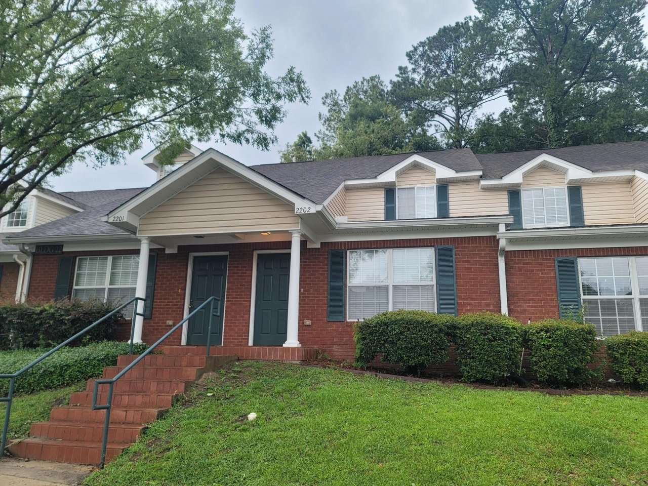 A charming brick home featuring a welcoming front porch and steps leading to the entrance.