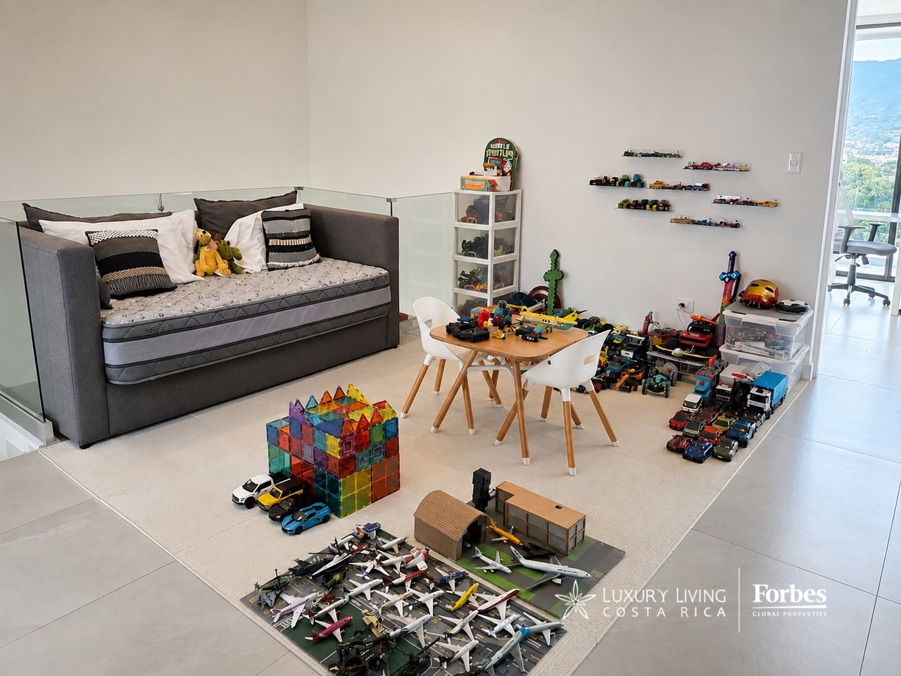 Children's playroom with a gray daybed, small table and chairs, and toys covering the floor.