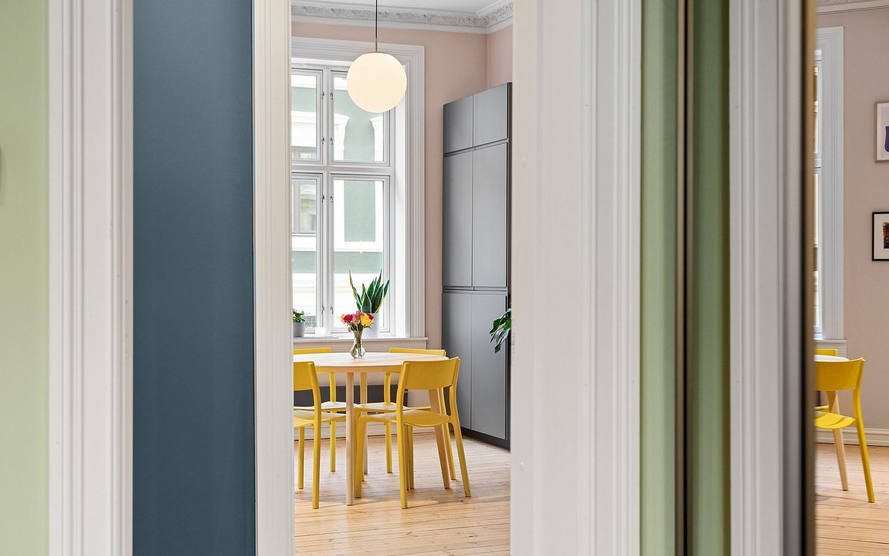 Dining area with yellow chairs, tall windows, and a built-in gray refrigerator.