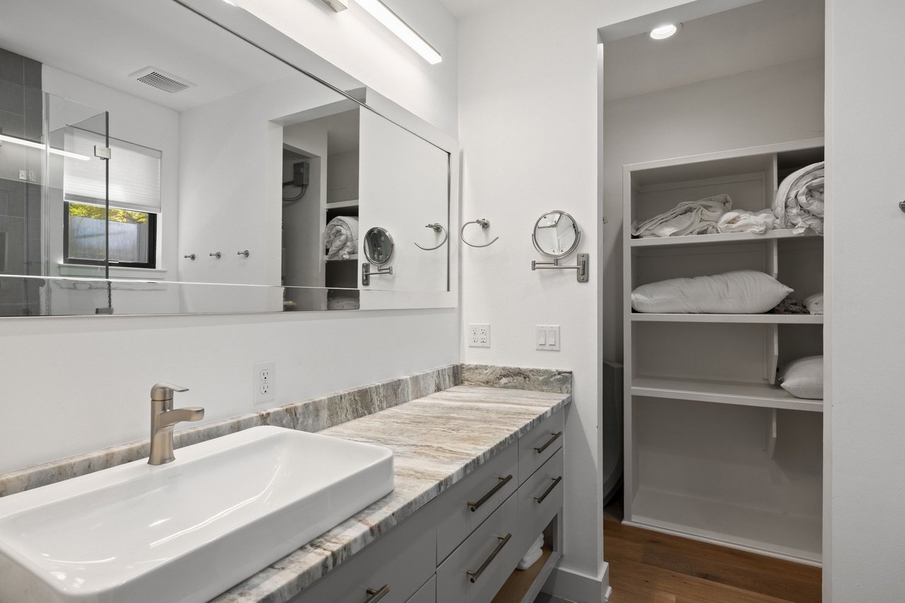 Bathroom with a vessel sink, stone-patterned counter, large mirror, and open linen shelving.