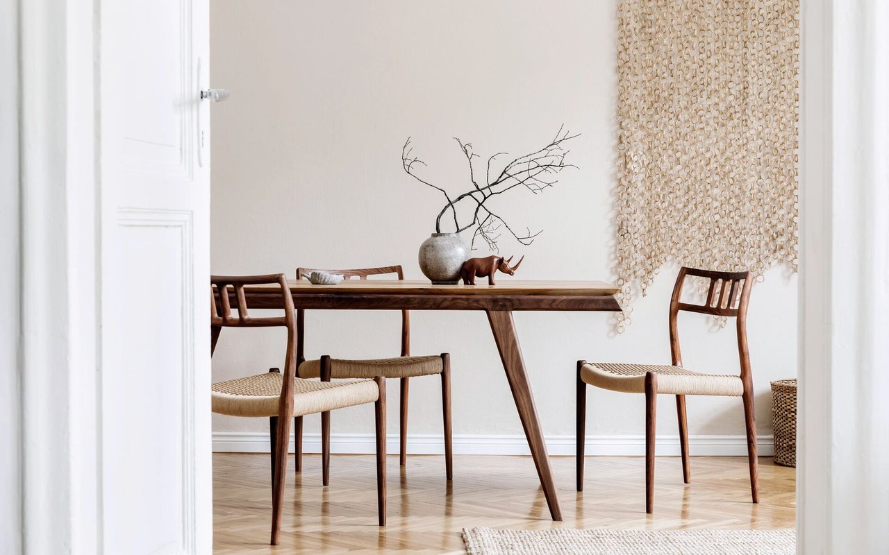 Dining room with a dark wood table, woven-seat chairs, and a ceramic vase of bare branches.