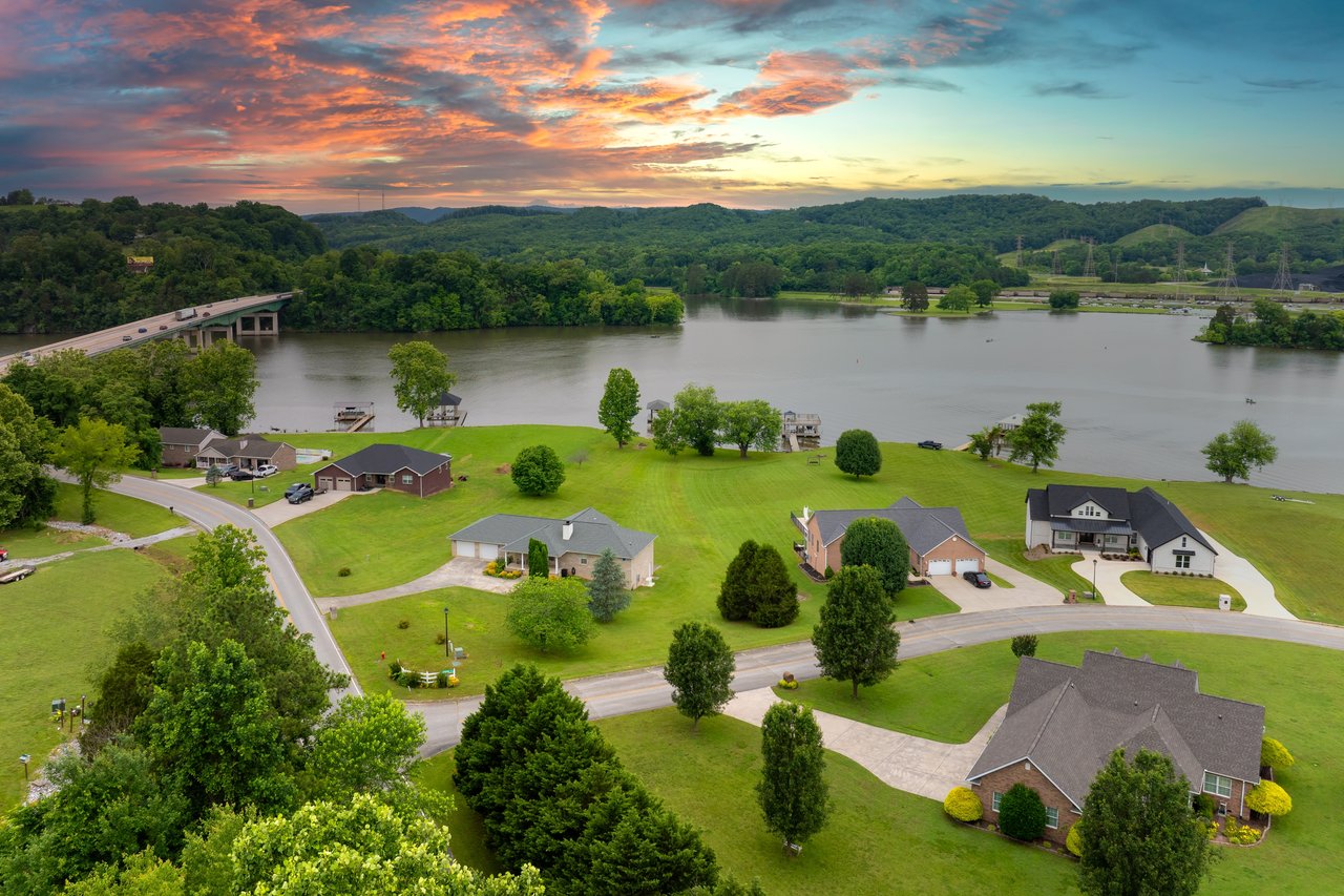 Aerial view of lakeside homes beside a bridge beneath a colorful sunset sky.
