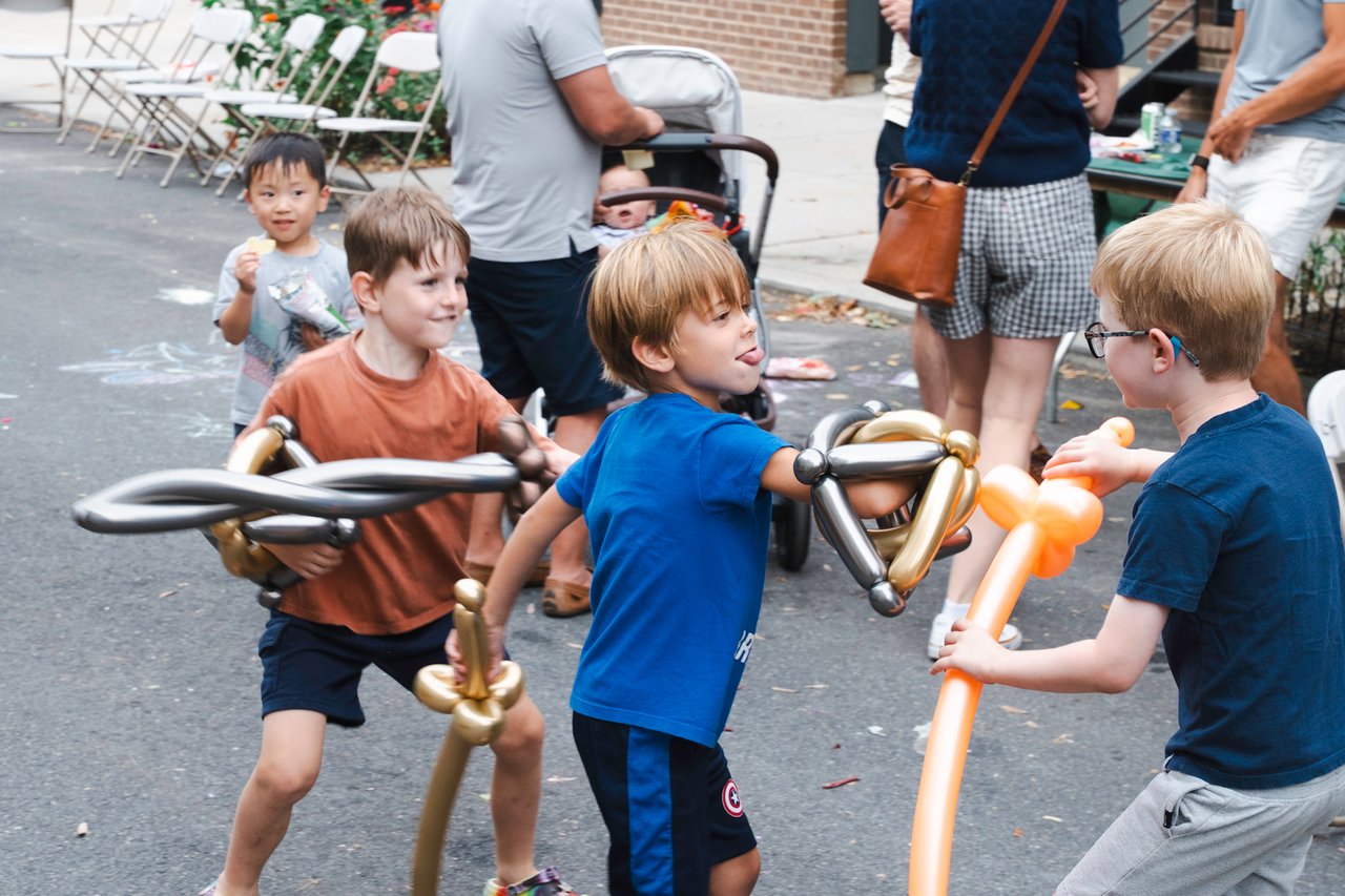 Children play with balloon creations at an outdoor neighborhood block party.