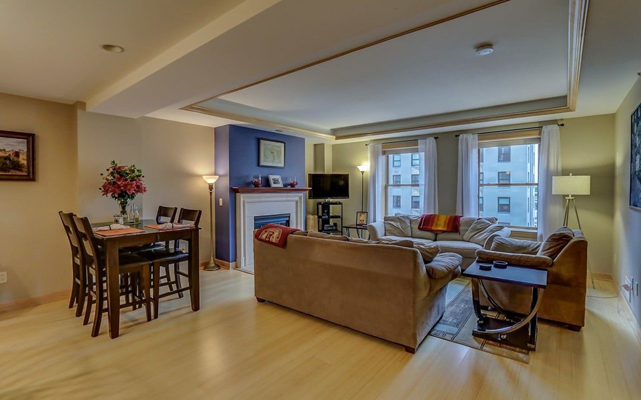 Urban condo living and dining area with a fireplace, sectional sofa, and large windows overlooking neighboring buildings.