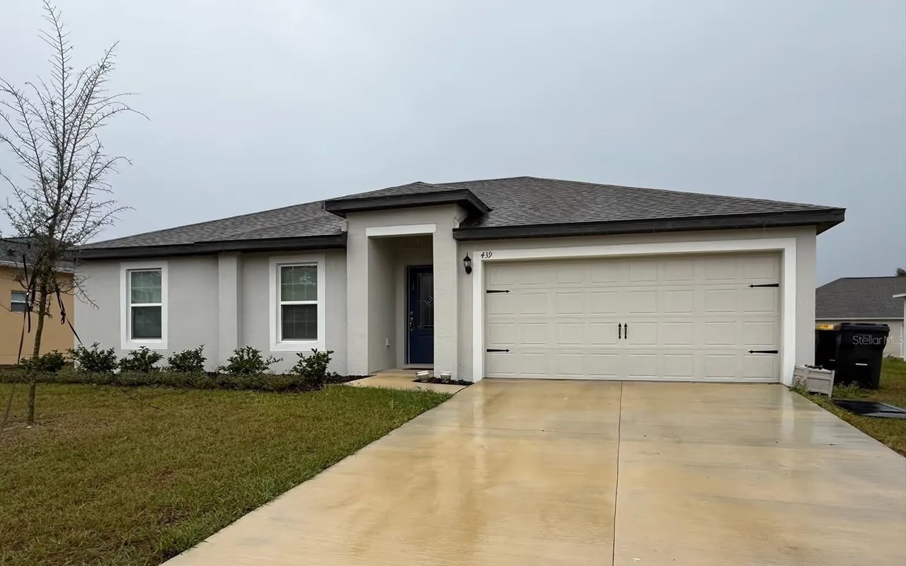Single-story stucco home with a dark roof, double garage, and broad concrete driveway.
