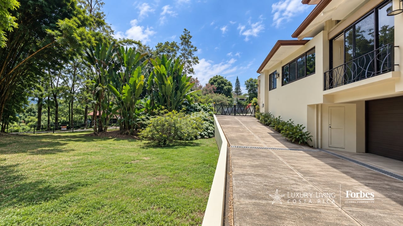 Modern two-story home beside a landscaped lawn, with a broad driveway and upper balcony.