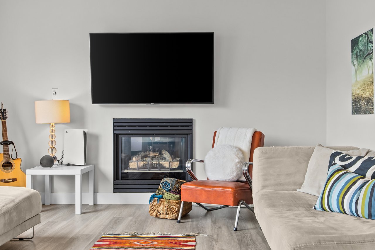 Living room with a gas fireplace, wall-mounted television, cream sofas, and an orange leather chair.