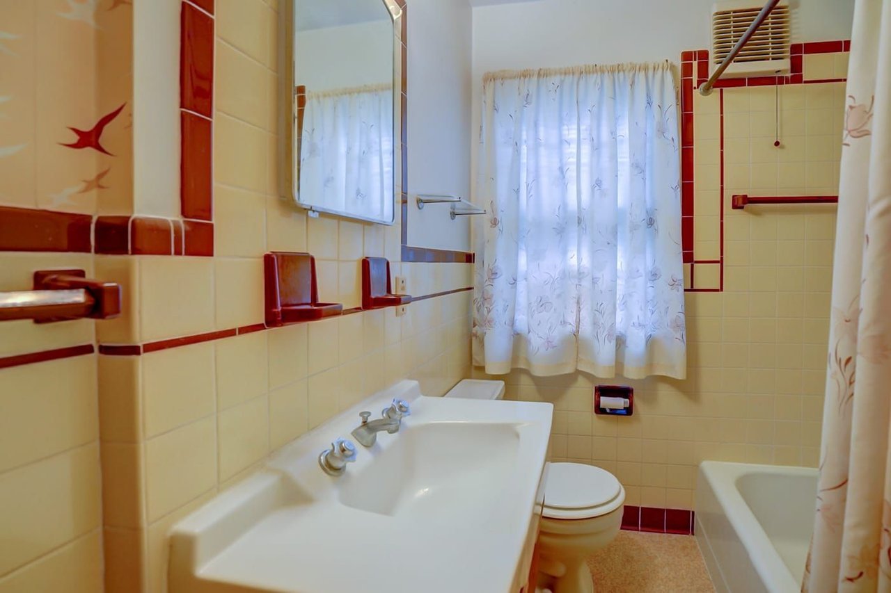 Vintage bathroom with cream-and-red tile, pedestal sink, and floral shower curtain