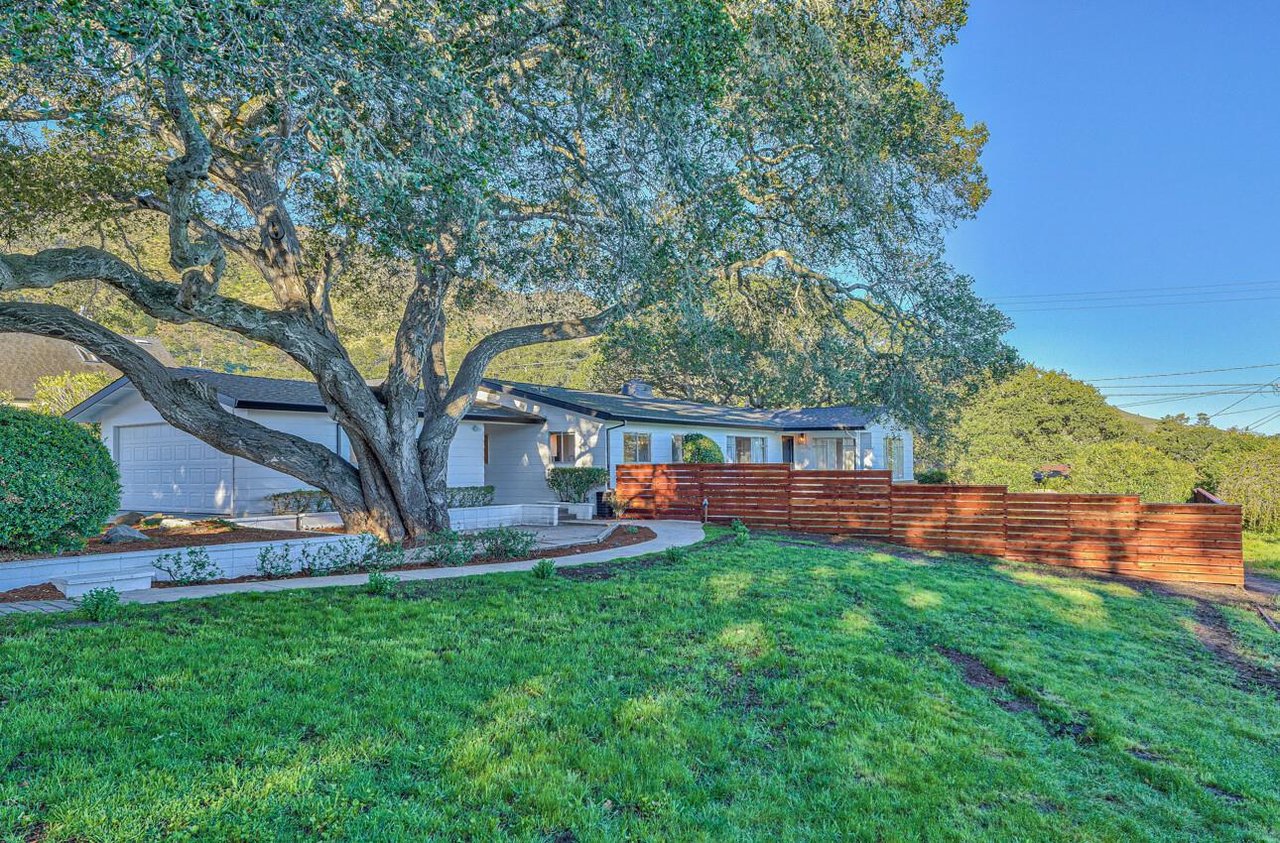 Single-story home with an attached garage, shaded by a large oak and bordered by a reddish wooden fence.