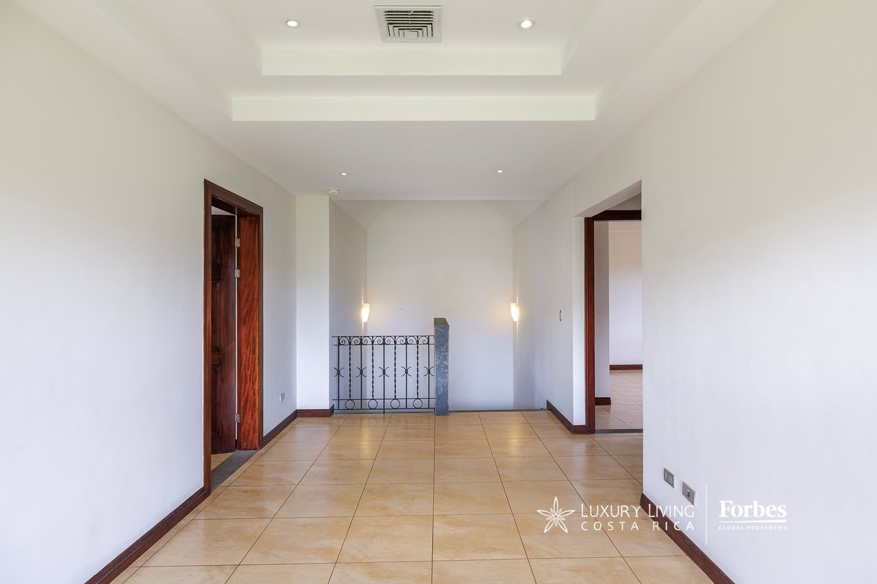 Empty tiled hallway with dark wood doorframes and a decorative railing beside the stairwell.