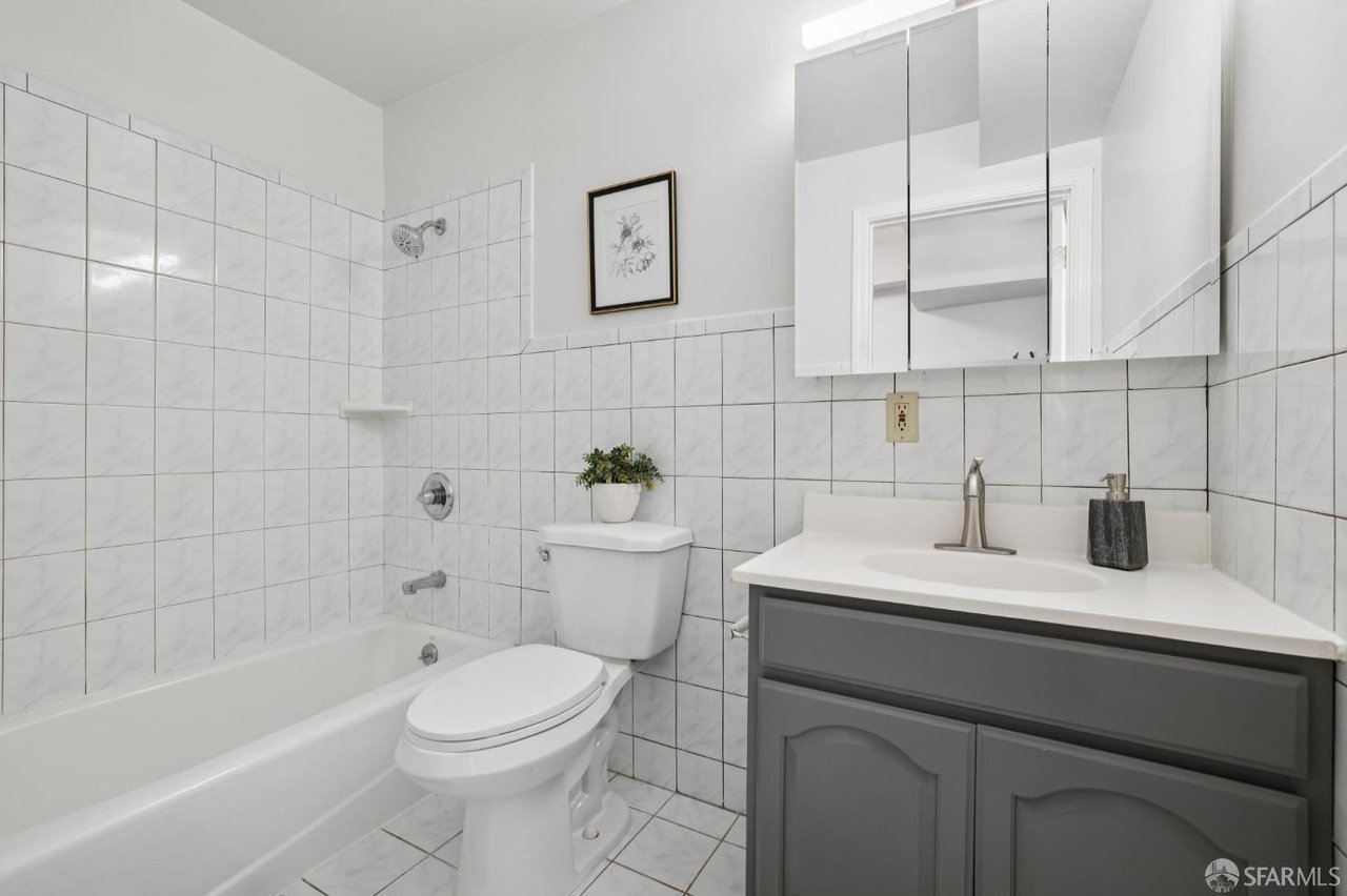Bathroom with a white tiled tub and shower, toilet, and gray vanity with mirrored cabinet.