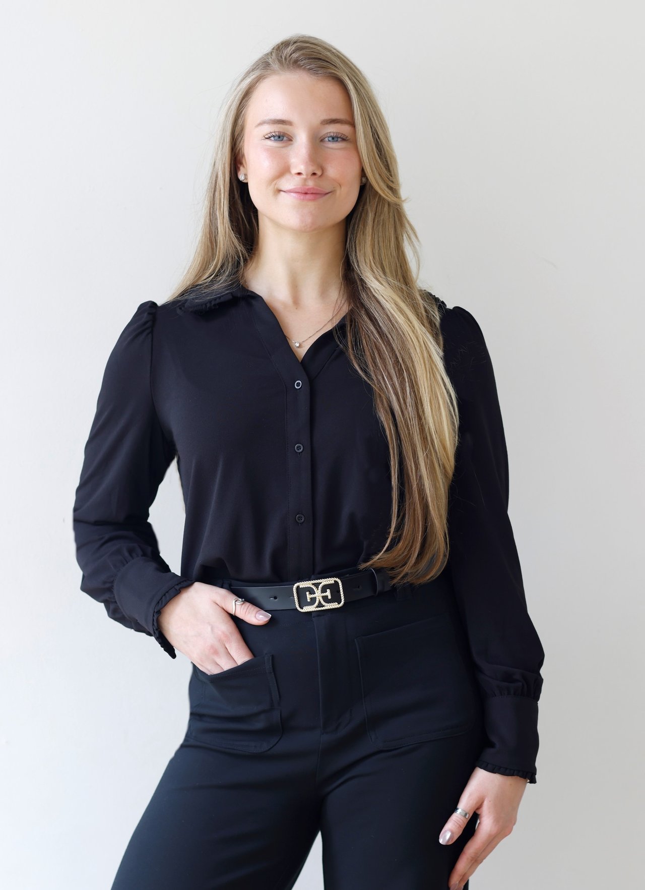 Bridget Neri in a black outfit, with long blonde hair against a light wall.