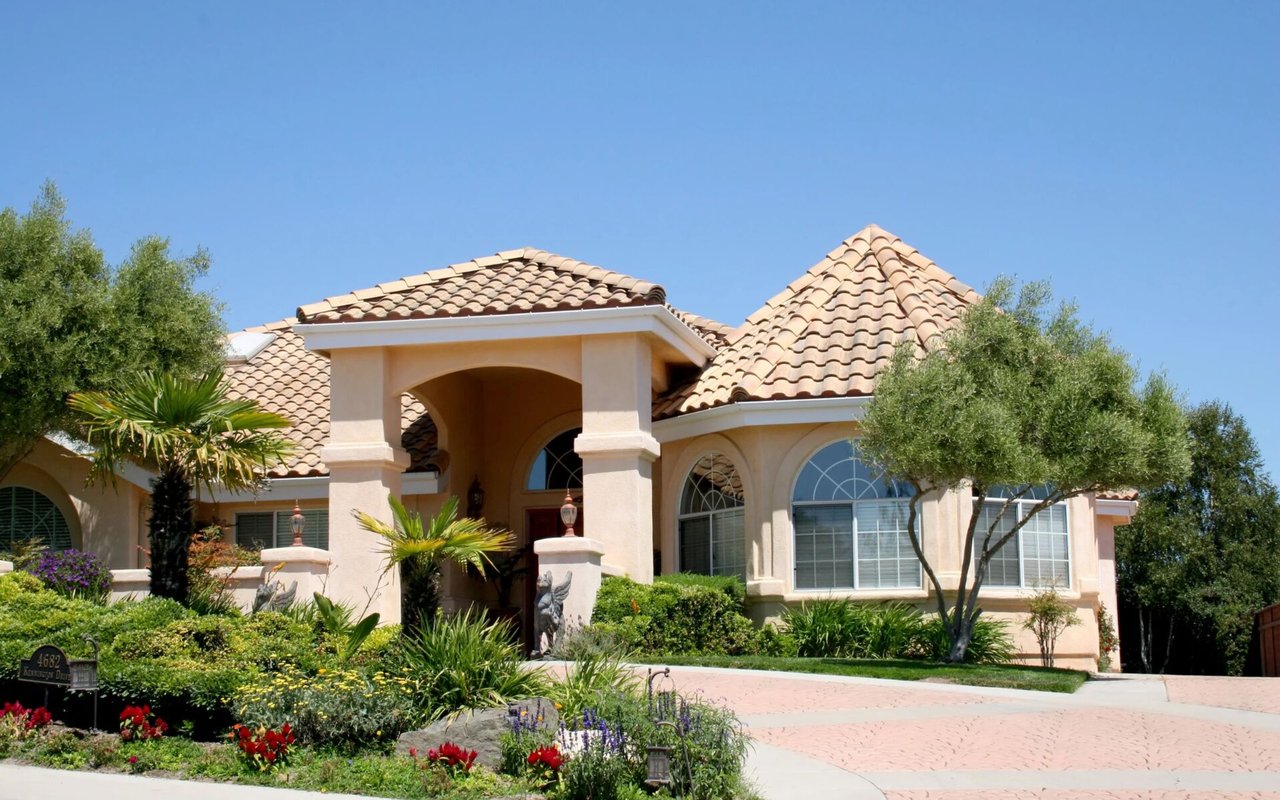 Stucco house with terracotta tile roofs, an arched entry, and a landscaped brick driveway.