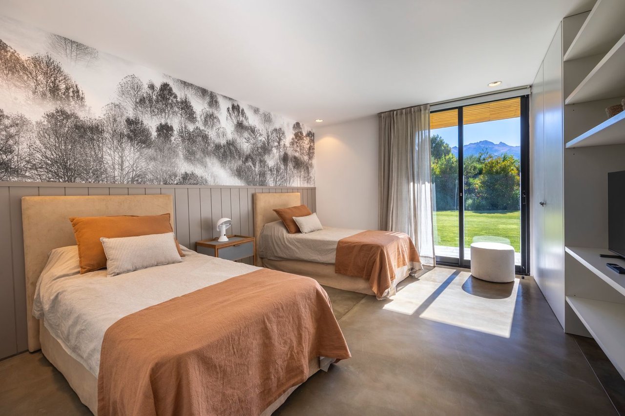 Bedroom with two single beds, a forest mural, and mountain views through glass doors.