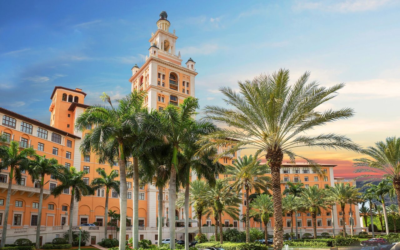 The Biltmore Hotel’s ornate tower rises above palm trees and peach-colored buildings.