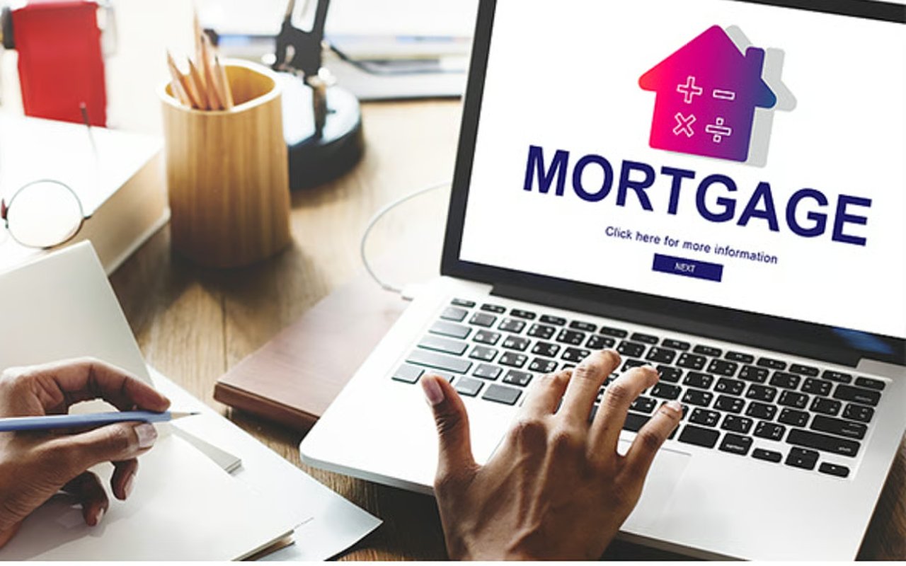 Person uses a laptop displaying a mortgage screen while writing on papers at a desk.
