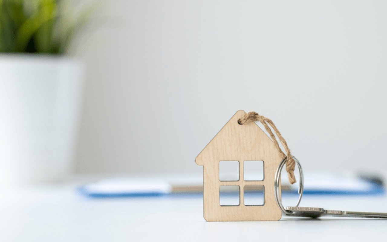 A house-shaped wooden keychain and metal key rest on a white surface.