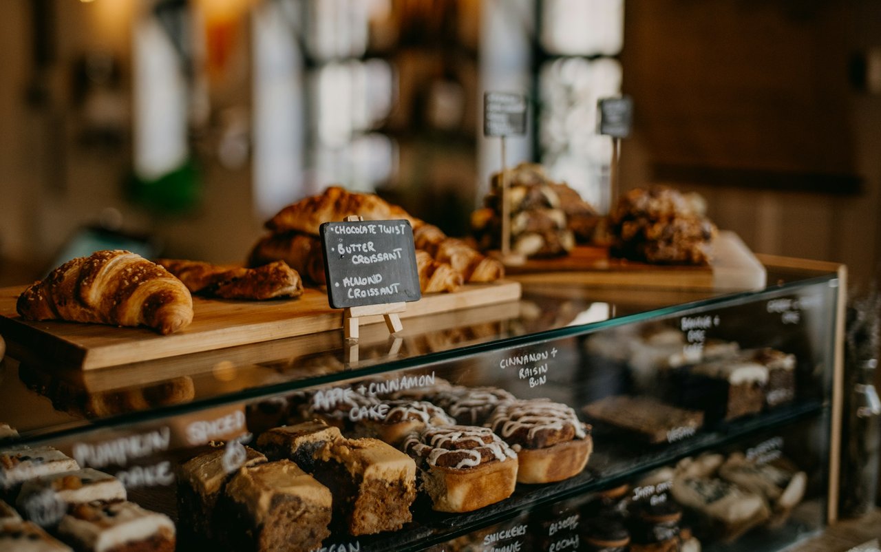 Bakery display case with croissants and cinnamon rolls, labeled on a small chalkboard.