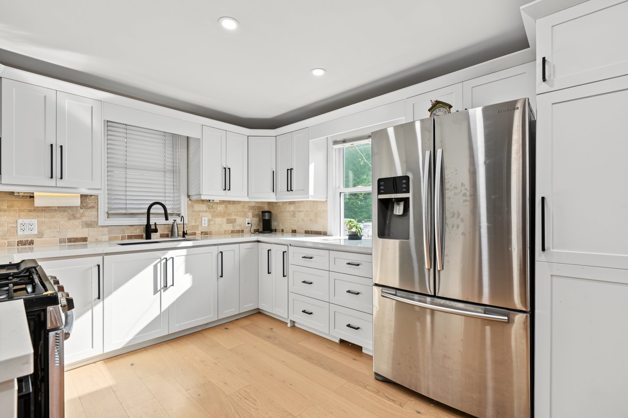 Bright kitchen with white cabinetry, a stainless steel refrigerator, stone tile backsplash, and light wood floors.
