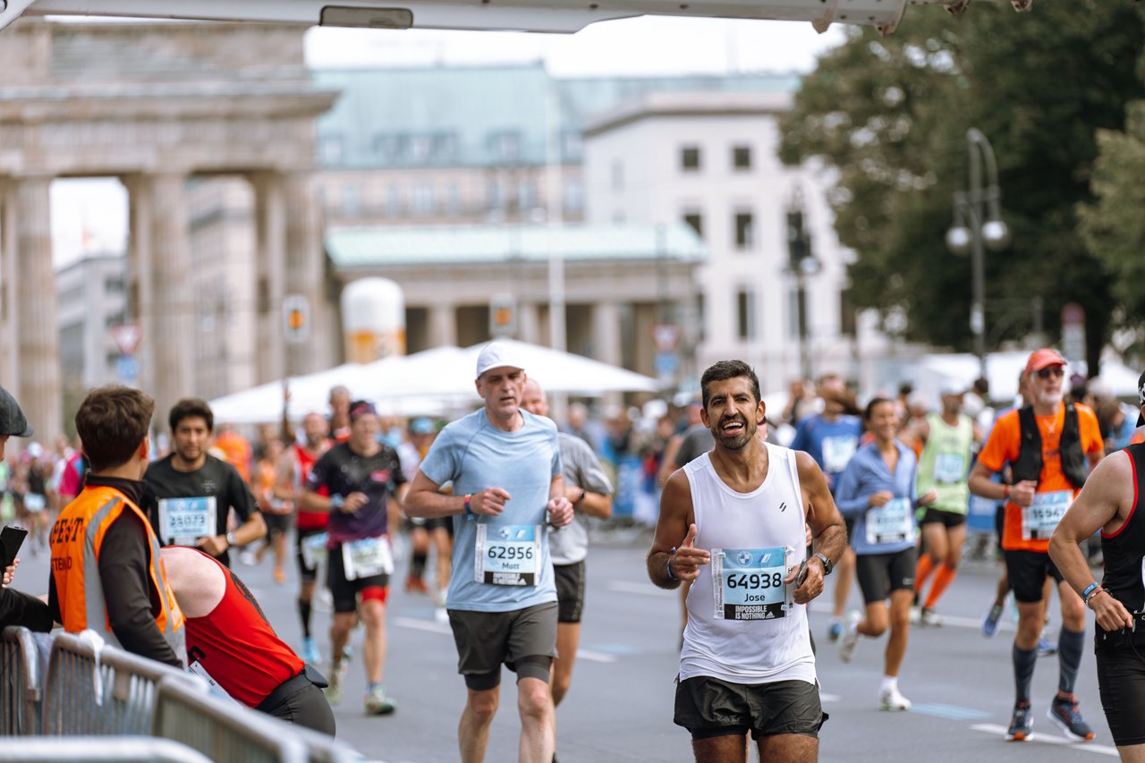 A panoramic photograph of thousands of New York City Marathon runners traveling along First Avenue on Manhattan's Upper East Side, with spectators cheering from both sidewalks and residential buildings lining the avenue.