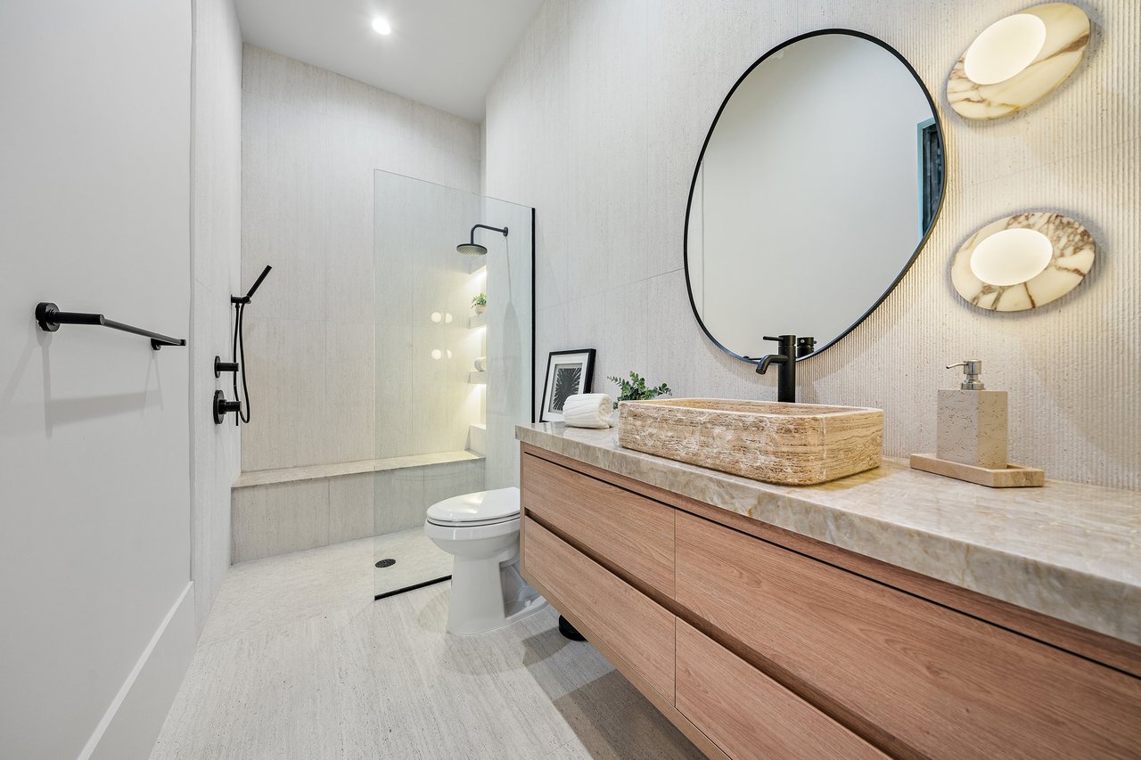 Modern bathroom with a stone vessel sink, wood vanity, oval mirror, and glass-enclosed shower.