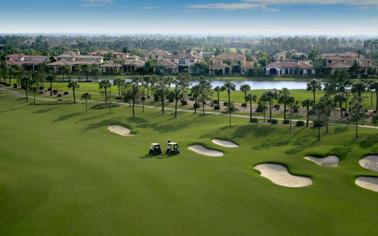Aerial view of a golf course with sand bunkers, golf carts, and homes beside a pond.