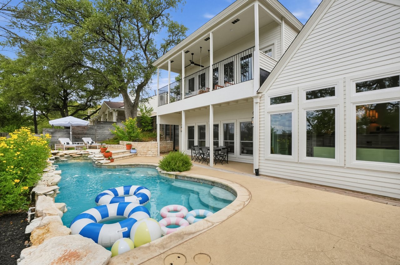 Backyard pool beside a white two-story home with a covered balcony and stone edging.