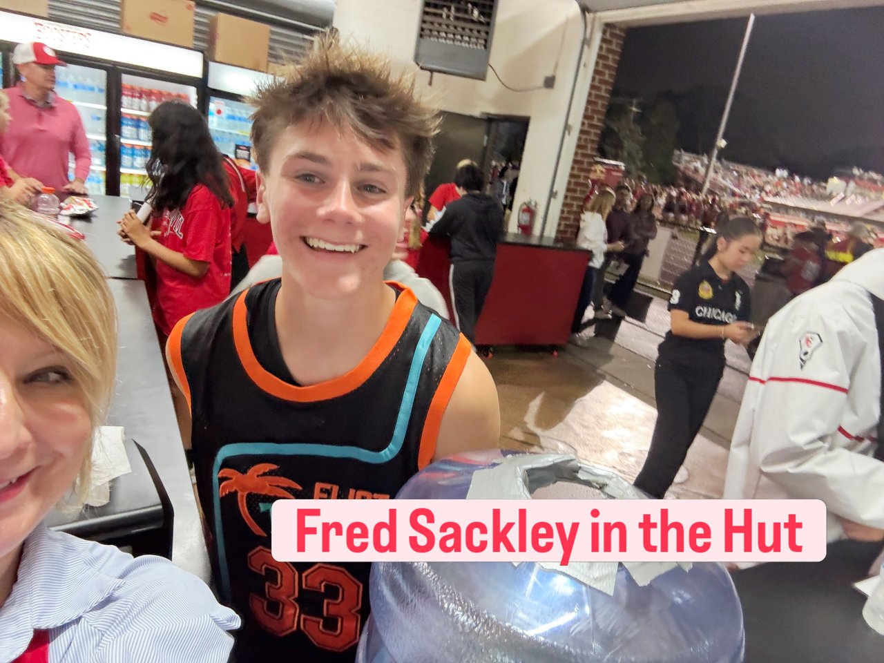 Fred Sackley smiles in a black-and-orange jersey inside a stadium concession hut.