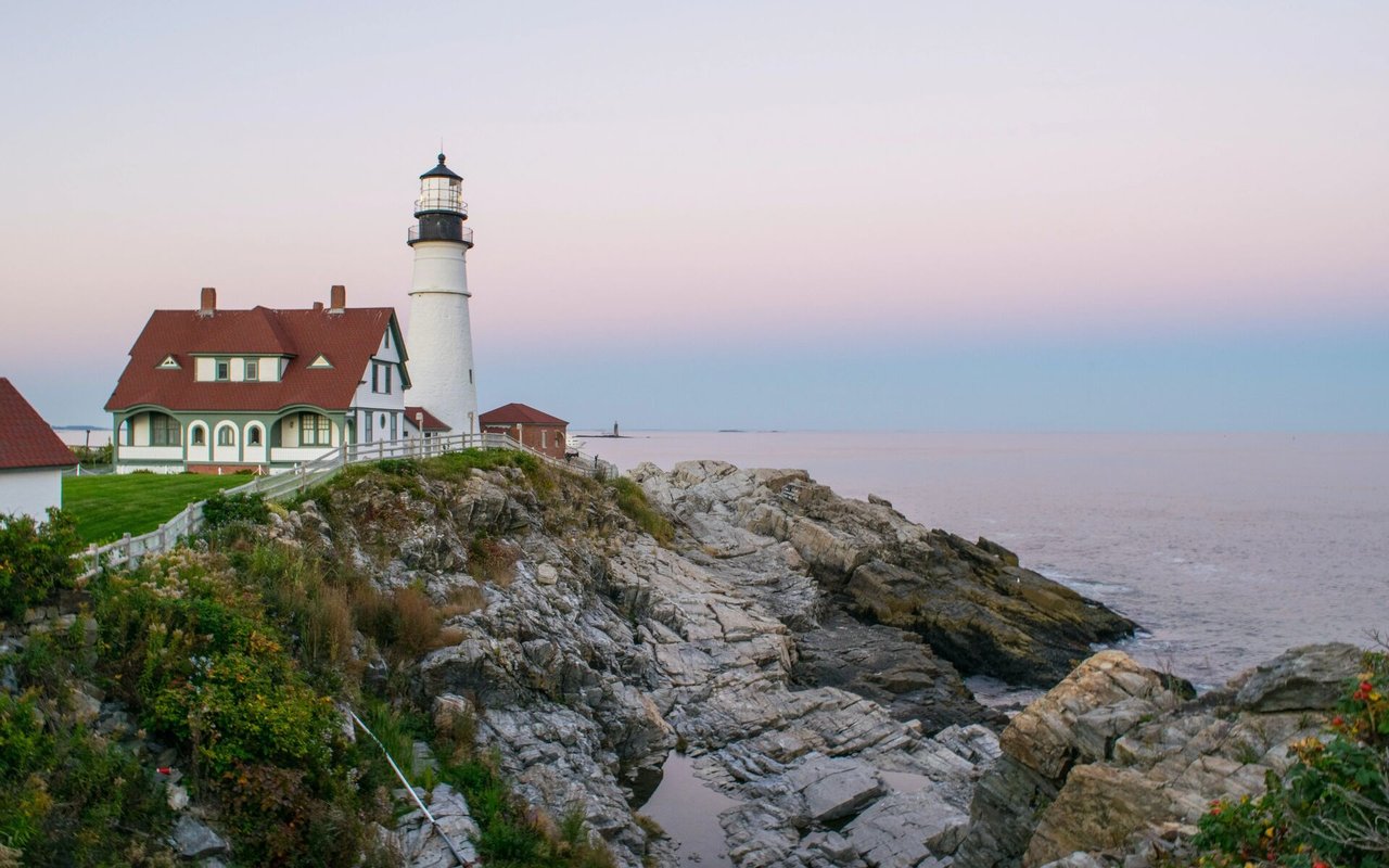Portland Head Light and its keeper’s house overlook a rocky shoreline at dusk.