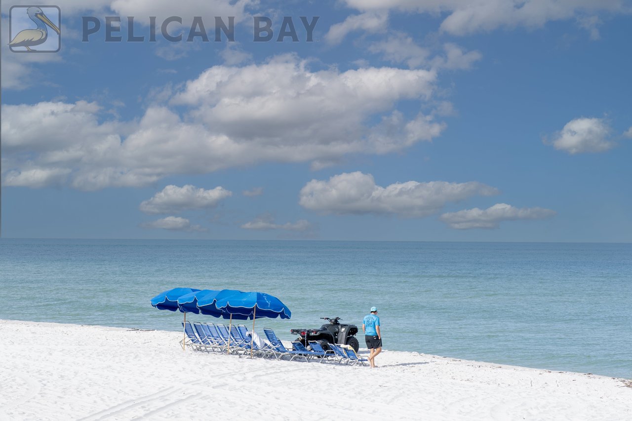 White sand beach in Pelican Bay Naples FL with blue umbrellas and private chair service along the Gulf