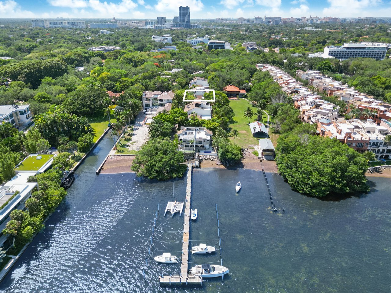 Aerial view of a white-outlined waterfront home among trees, with a canal and boats in the foreground.