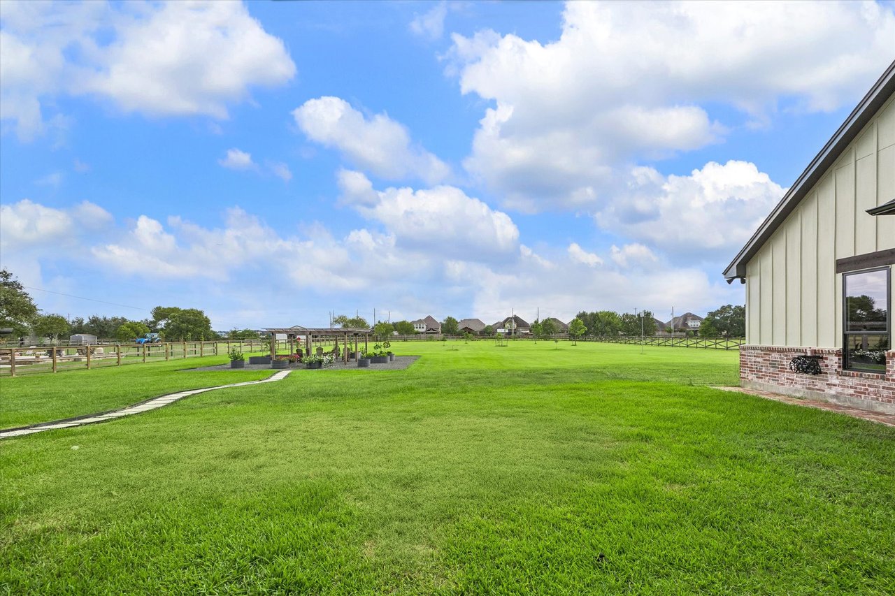 Spacious green backyard with fenced grounds, garden beds beneath a pergola, and the home at right.