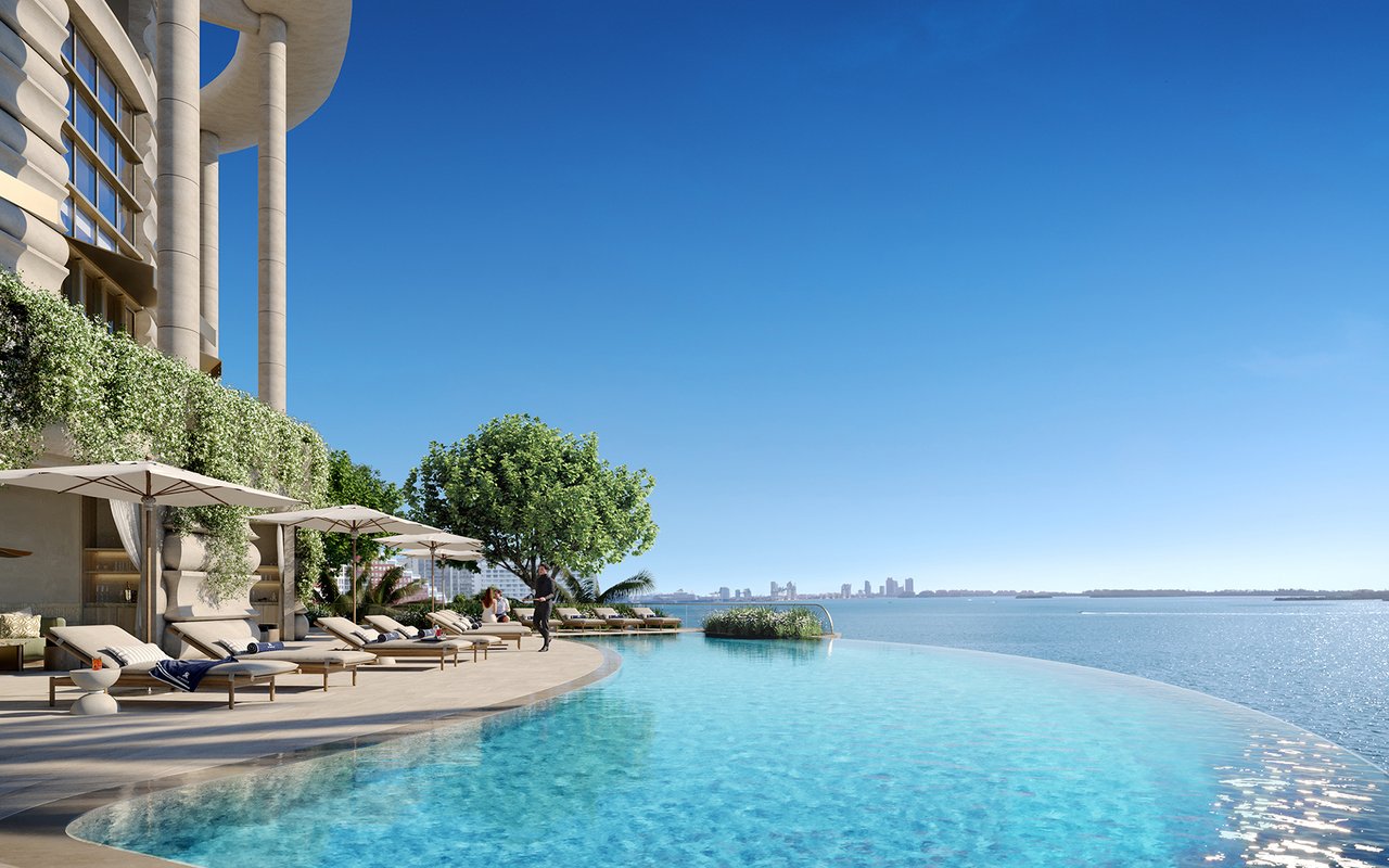 Waterfront infinity pool beside the St. Regis Residences terrace, with loungers and the Miami skyline beyond.