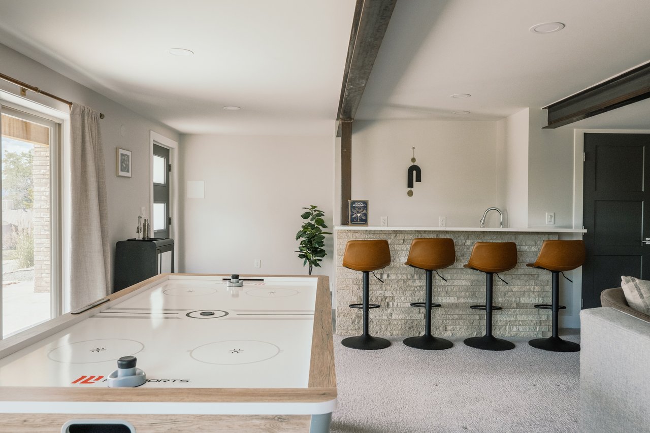 Game room with a white tabletop game and a stone-front bar lined with four brown stools.