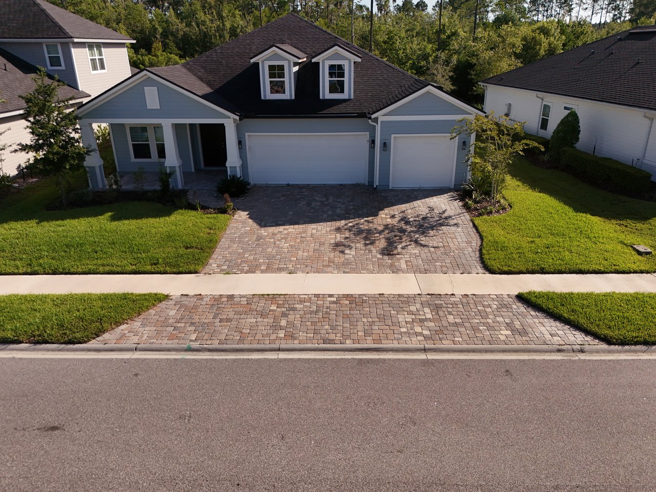 Blue-gray two-story home with dormers, a three-car garage, and a wide paver driveway.