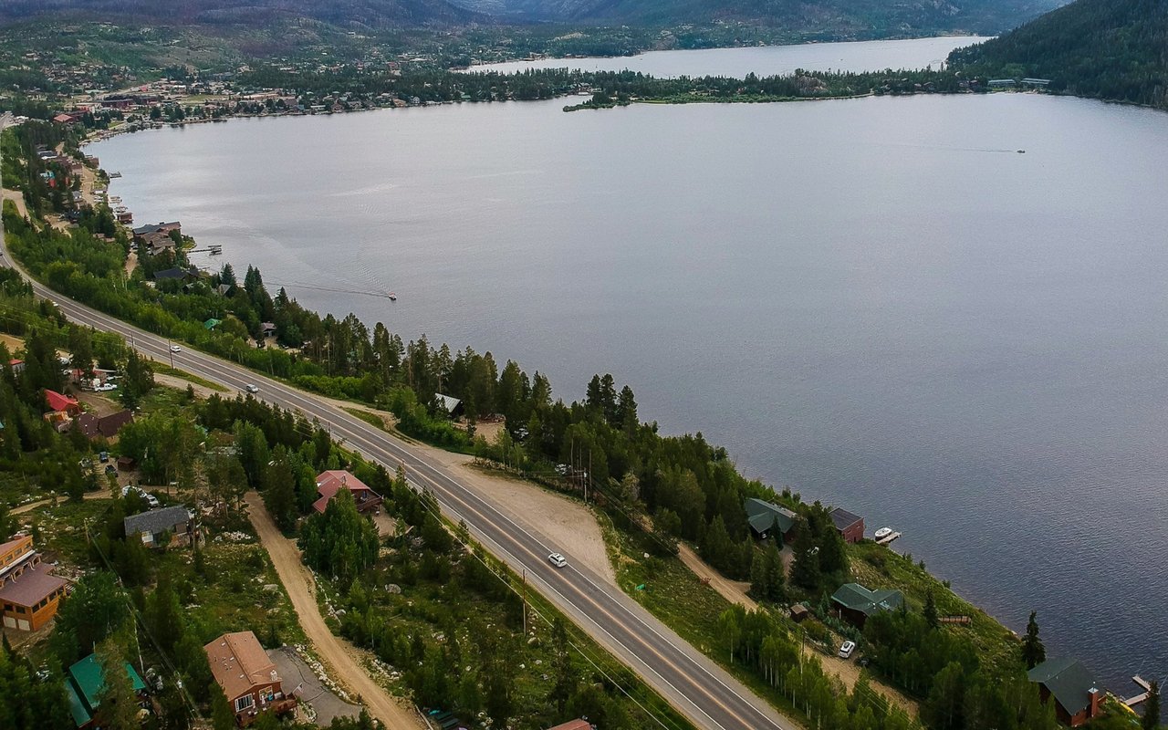 Aerial view of a lakeside community with a shoreline highway and mountains beyond.