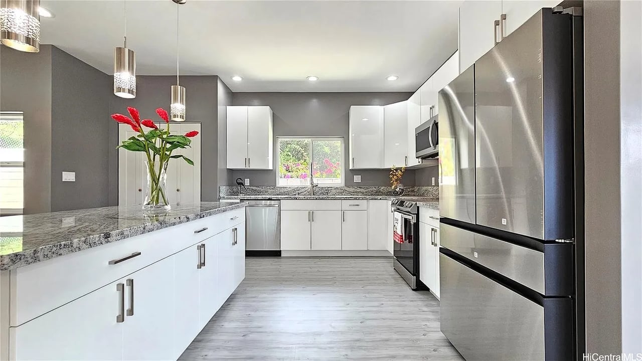Bright white kitchen with a granite island, stainless steel appliances, and red flowers.