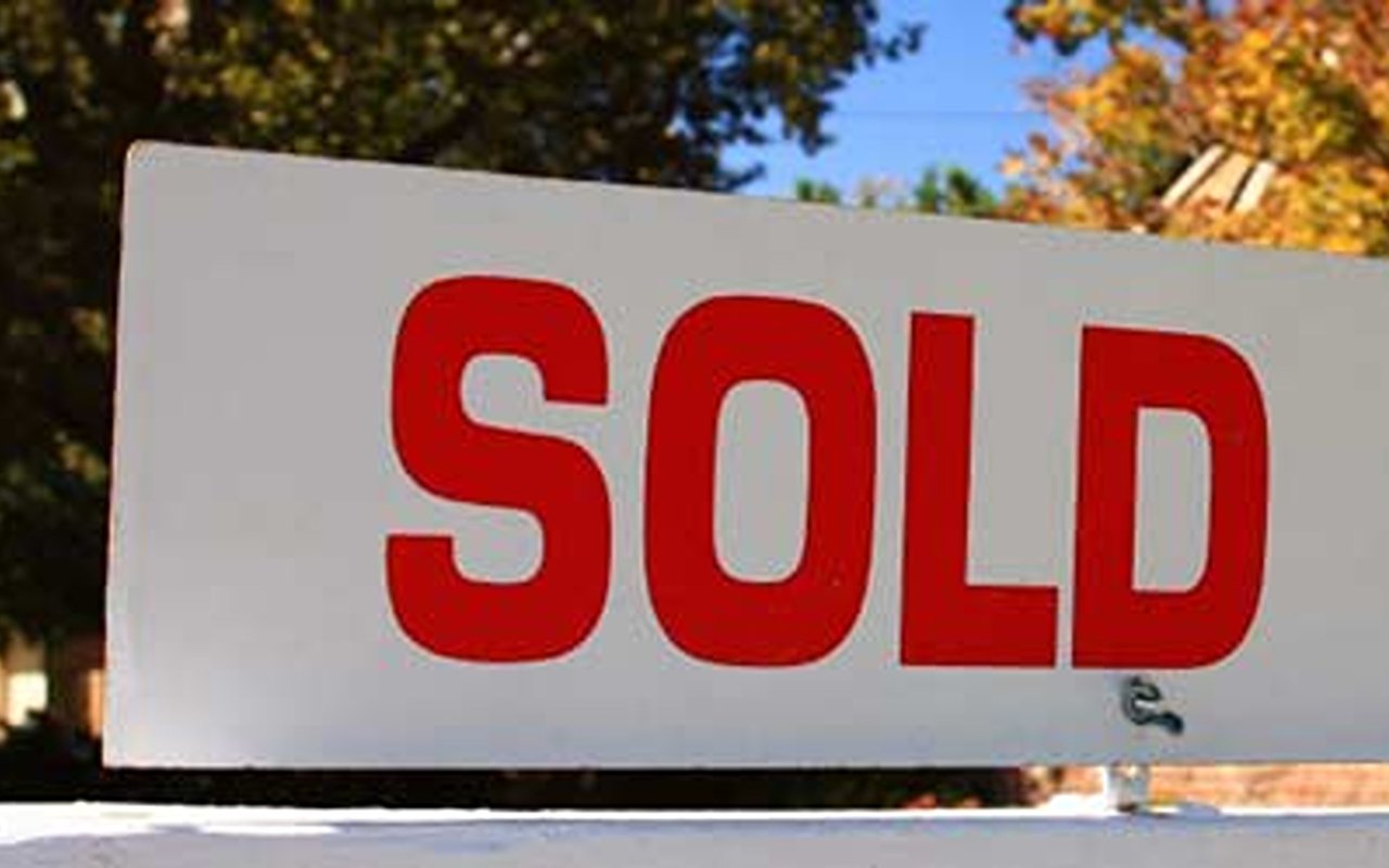 A real estate sign marked SOLD against autumn trees.