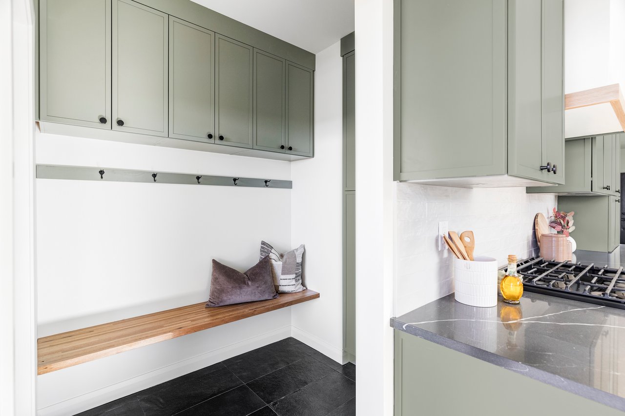 Mud room and additional storage space for pantry with sage-colored cabinets, hooks, and a wood bench