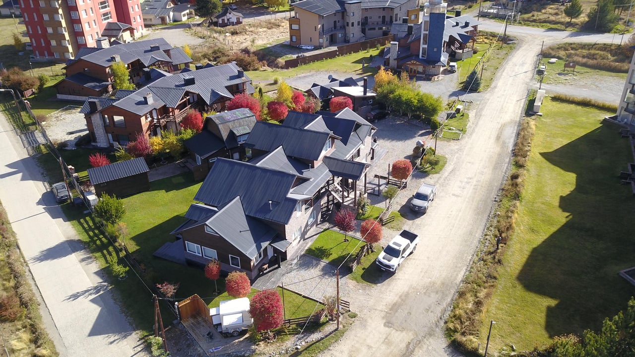 Aerial view of chalet-style homes along a gravel road, with colorful autumn trees and parked vehicles.